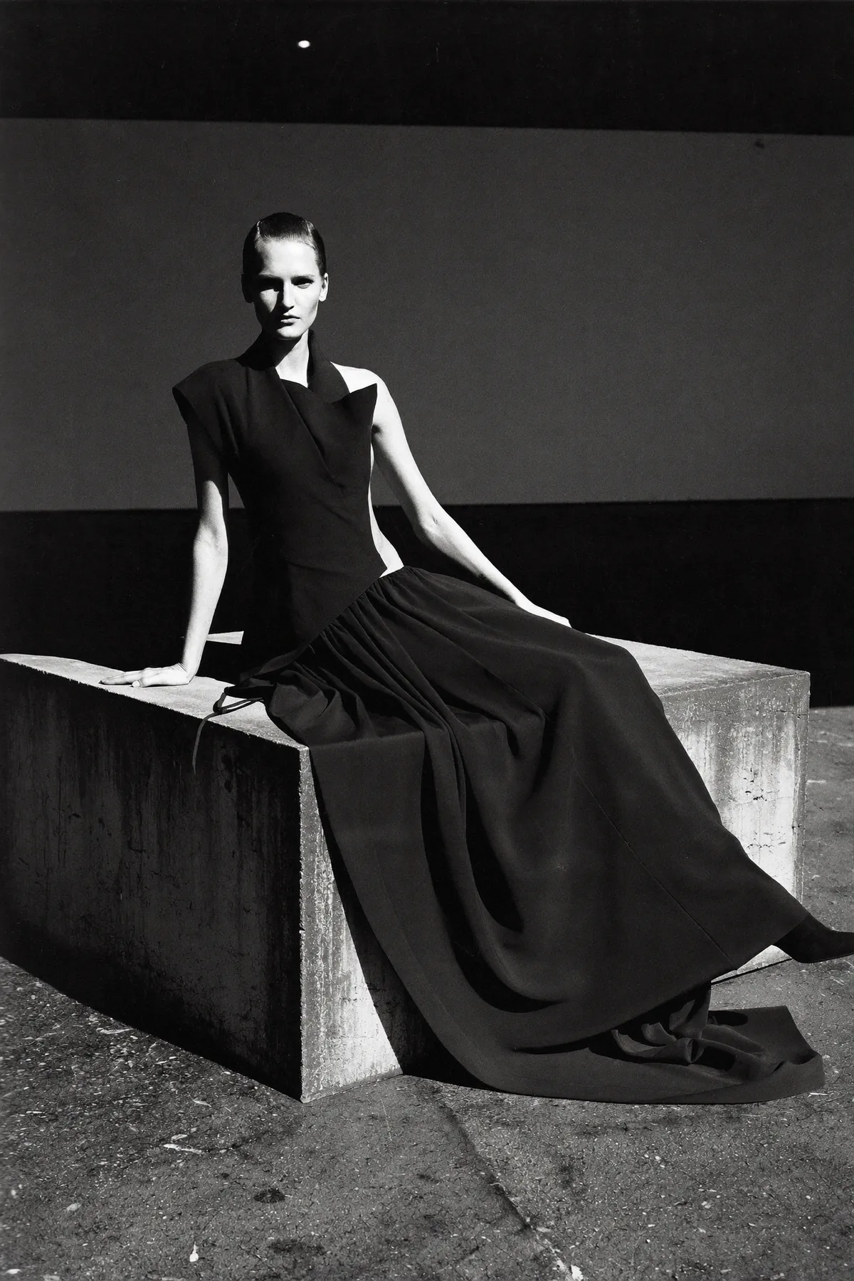 Model seated on concrete, gown spread